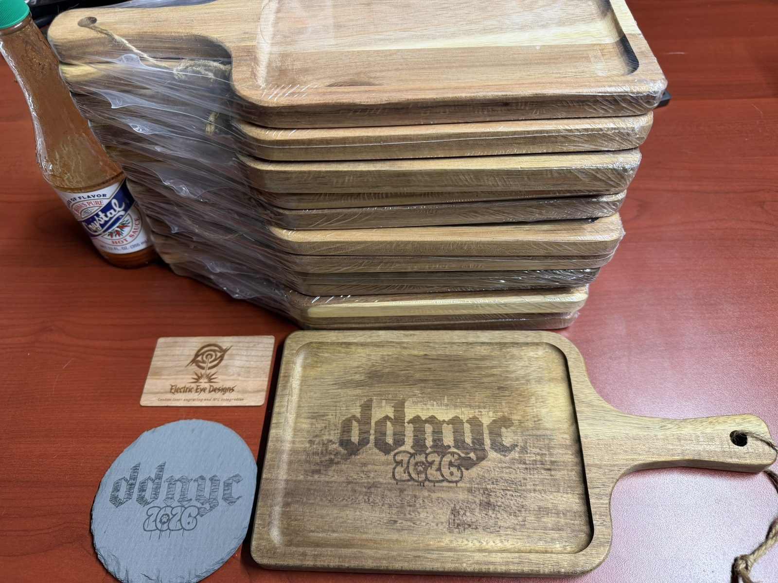 Walnut serving boards engraved with DDNYC 2026, plus a matching slate coaster and branded wood card