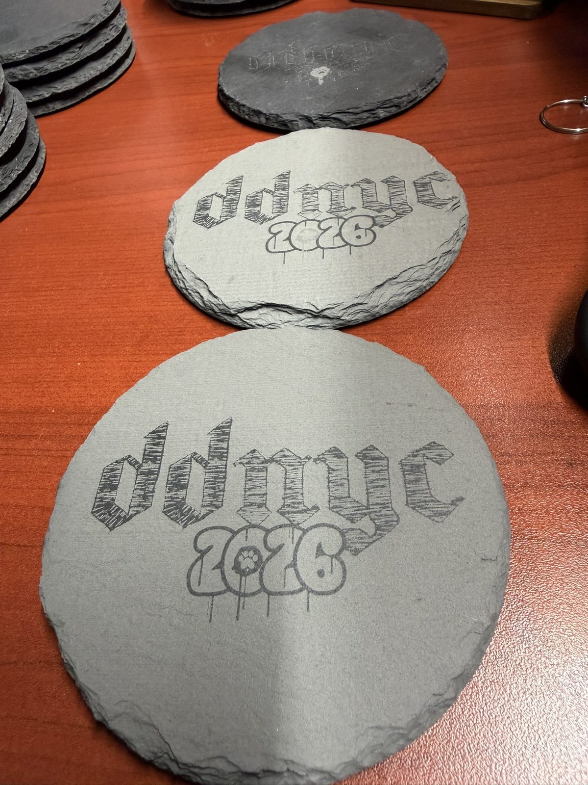 Round slate coasters engraved with gothic DDNYC 2026 lettering