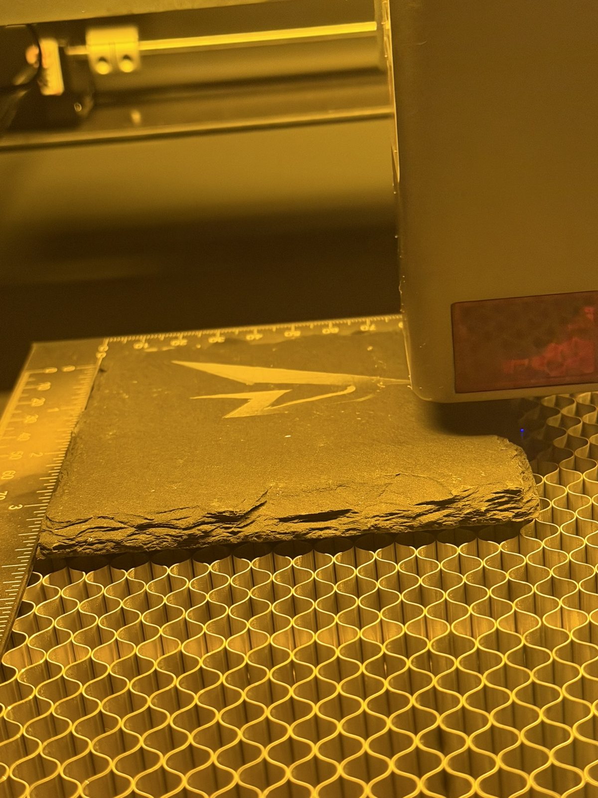 Slate tile on the honeycomb bed being engraved with a lightning bolt